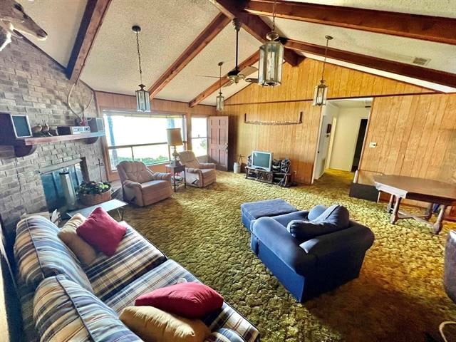 carpeted living room featuring vaulted ceiling with beams, ceiling fan, and wood walls