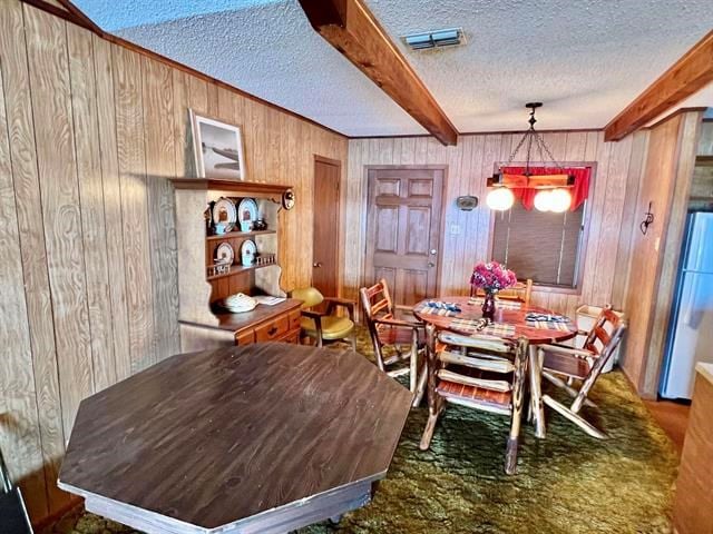 dining space featuring beam ceiling, wooden walls, dark carpet, and a textured ceiling