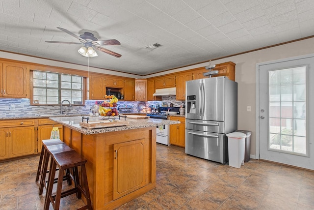 kitchen featuring white range, stainless steel refrigerator with ice dispenser, decorative backsplash, a kitchen island, and a kitchen bar