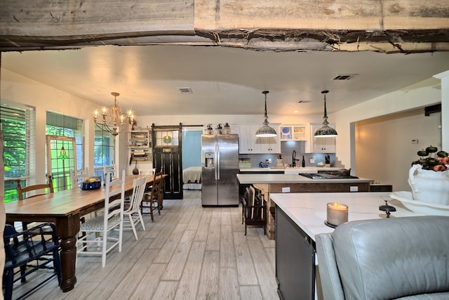 kitchen featuring white cabinetry, hanging light fixtures, light hardwood / wood-style floors, stainless steel fridge with ice dispenser, and a barn door