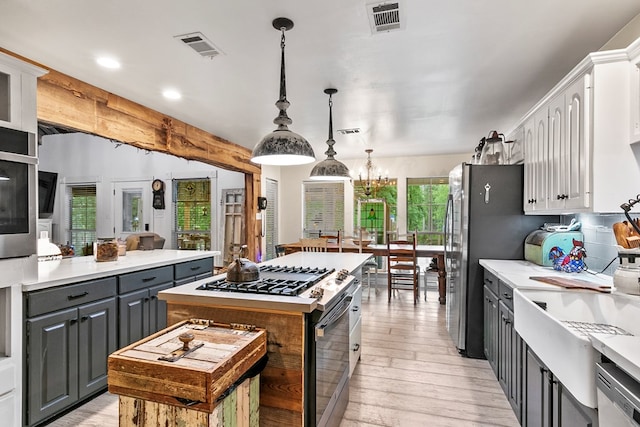 kitchen featuring gray cabinetry, hanging light fixtures, stainless steel appliances, a center island, and white cabinets