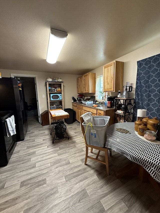 kitchen with light wood-type flooring, sink, black appliances, and a textured ceiling