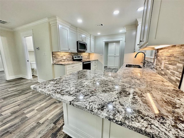 kitchen featuring kitchen peninsula, light stone counters, white cabinets, and appliances with stainless steel finishes