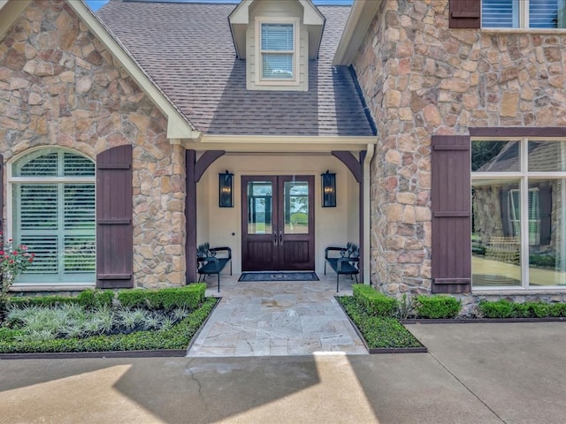 property entrance with french doors, stone siding, roof with shingles, and stucco siding