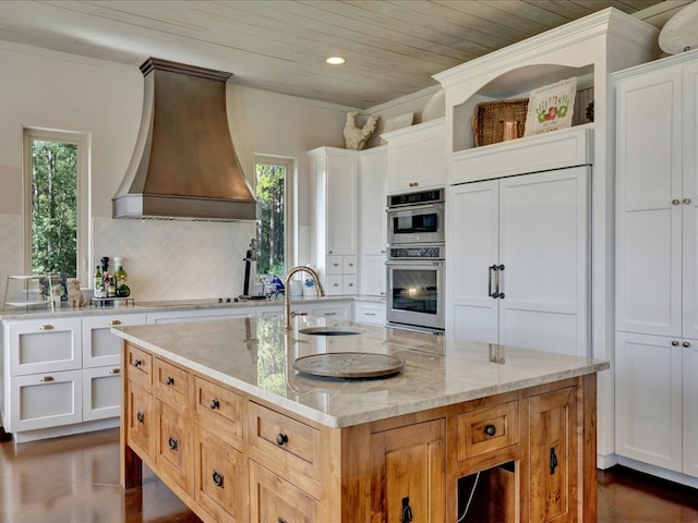 kitchen featuring light stone countertops, white cabinetry, a kitchen island with sink, and custom exhaust hood