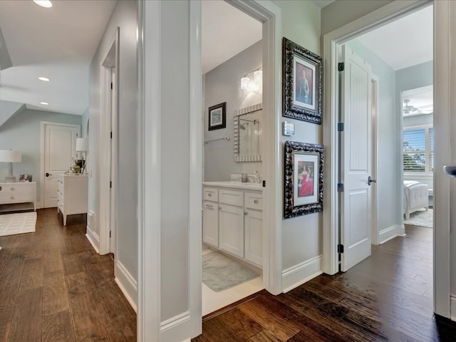 hall with dark wood finished floors, recessed lighting, baseboards, and a sink