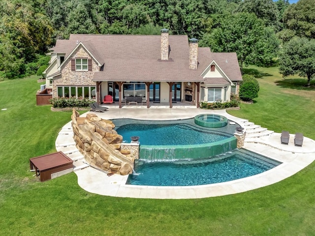 back of house with a patio, an in ground hot tub, a chimney, stone siding, and a lawn