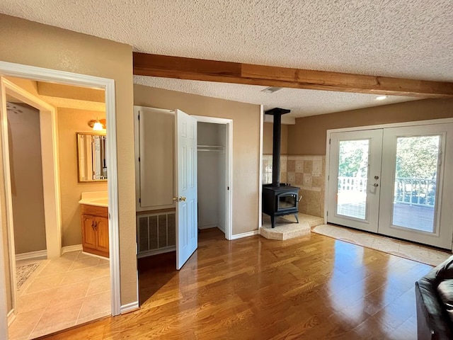 670 Cedar Crest Cir, Hemphill, TX 75948 - unfurnished living room with french doors, a textured ceiling, light wood-type flooring, a wood stove, and beamed ceiling