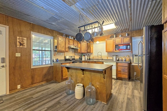 kitchen featuring appliances with stainless steel finishes, dark wood-type flooring, wooden walls, sink, and a center island