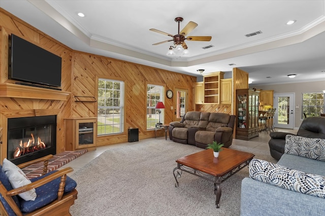 living room featuring light tile patterned floors, crown molding, ceiling fan, a tray ceiling, and wood walls