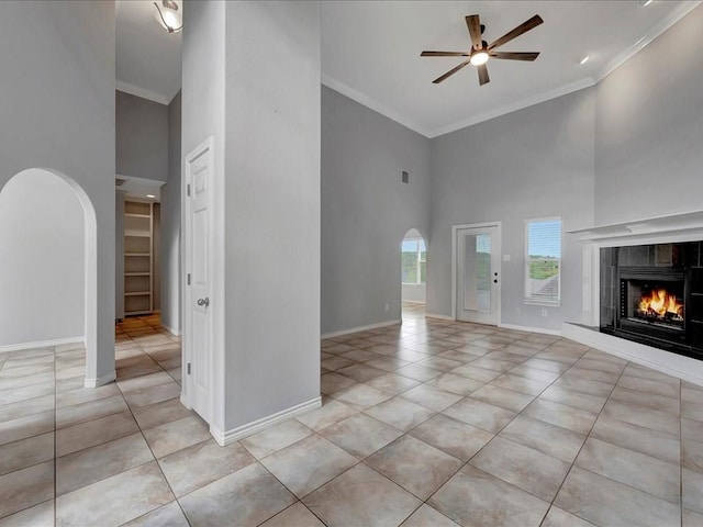 unfurnished living room featuring ceiling fan, a tile fireplace, crown molding, and a high ceiling