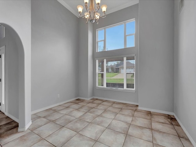 tiled spare room featuring a chandelier, a towering ceiling, and ornamental molding