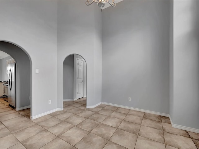 tiled empty room featuring a high ceiling and a chandelier