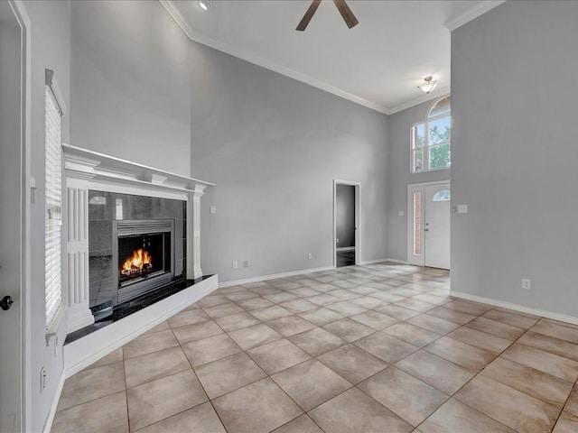 unfurnished living room featuring a tiled fireplace, crown molding, ceiling fan, and a high ceiling