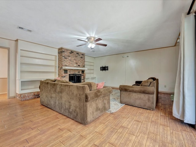 living room with built in shelves, light hardwood / wood-style floors, a brick fireplace, and ceiling fan