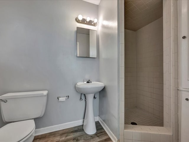 bathroom with hardwood / wood-style flooring, toilet, and tiled shower