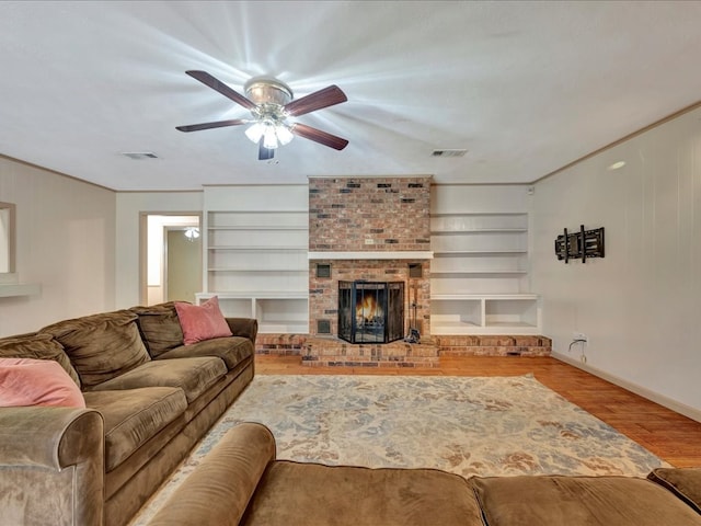 living room with hardwood / wood-style flooring, ceiling fan, crown molding, and a brick fireplace