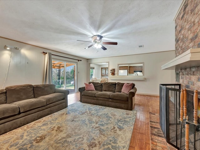 living room with a textured ceiling, dark hardwood / wood-style flooring, a brick fireplace, and ceiling fan