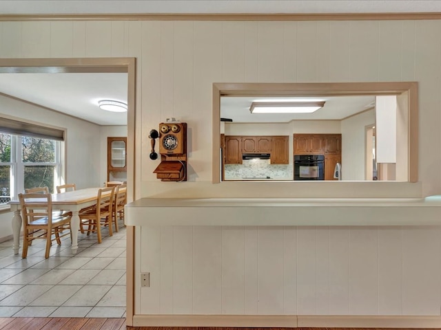 kitchen featuring black oven, light tile patterned flooring, and wooden walls