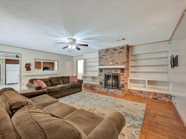 living room featuring ceiling fan, a brick fireplace, built in features, light hardwood / wood-style floors, and ornamental molding