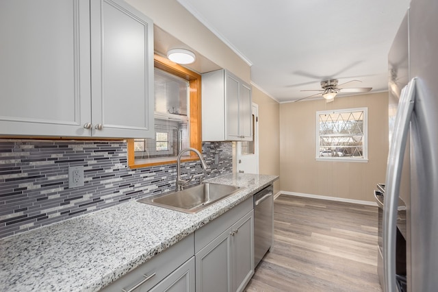 kitchen with sink, appliances with stainless steel finishes, ornamental molding, light stone countertops, and light wood-type flooring