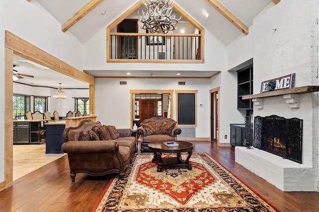 living room featuring beamed ceiling, high vaulted ceiling, hardwood / wood-style floors, a fireplace, and ceiling fan with notable chandelier