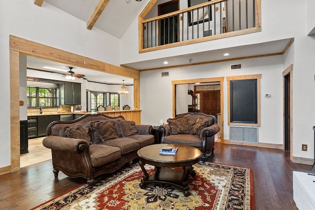 living room with beam ceiling, ceiling fan with notable chandelier, a high ceiling, and wood-type flooring