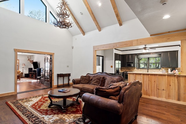 living room featuring dark hardwood / wood-style flooring, ceiling fan with notable chandelier, sink, high vaulted ceiling, and beamed ceiling