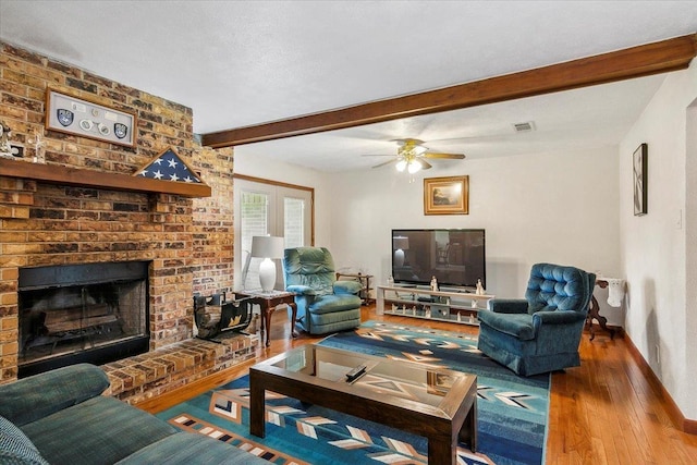 living room with ceiling fan, a fireplace, beamed ceiling, and hardwood / wood-style flooring