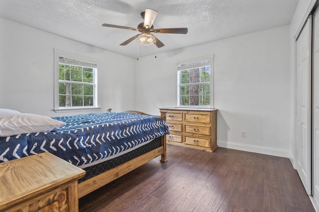 bedroom with multiple windows, dark wood-type flooring, a closet, and ceiling fan