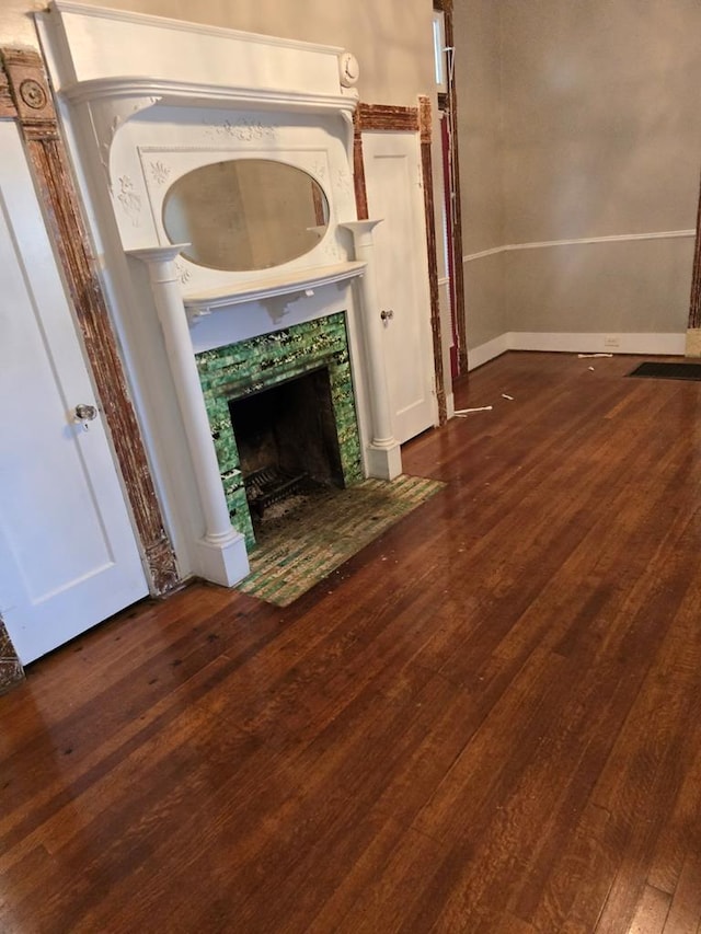 unfurnished living room featuring baseboards, decorative columns, a tiled fireplace, and hardwood / wood-style flooring