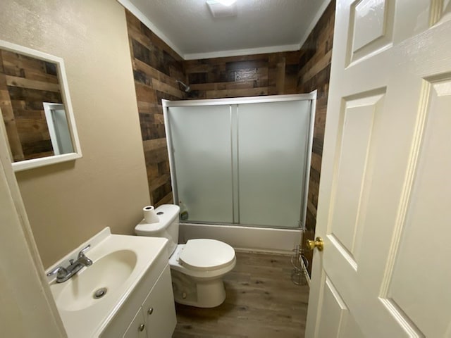 full bathroom featuring combined bath / shower with glass door, vanity, hardwood / wood-style flooring, toilet, and wood walls