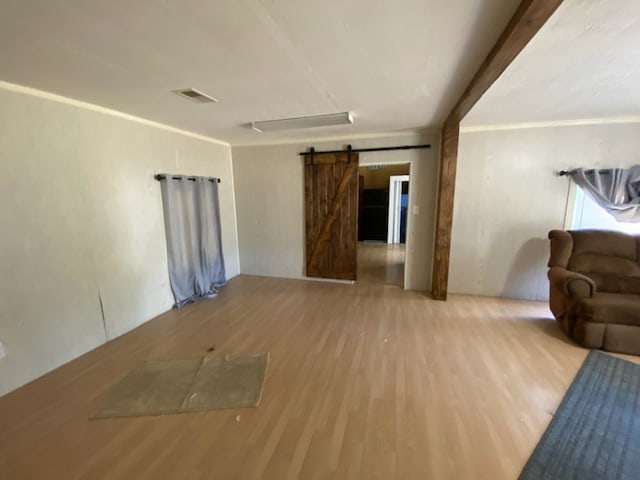 unfurnished living room featuring light wood-type flooring, a barn door, and ornamental molding