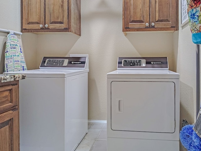 laundry area featuring washer and dryer, baseboards, cabinet space, and light tile patterned floors