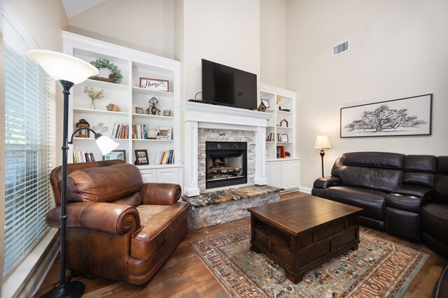living area with visible vents, built in shelves, high vaulted ceiling, wood finished floors, and a fireplace