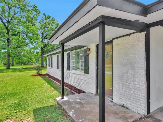 view of side of property featuring a lawn, a patio, and brick siding