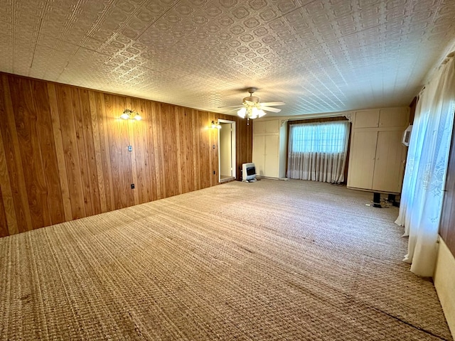 unfurnished room with carpet flooring, ceiling fan, wood walls, and heating unit