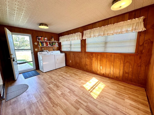 laundry room with a textured ceiling, washing machine and dryer, light hardwood / wood-style flooring, and wooden walls