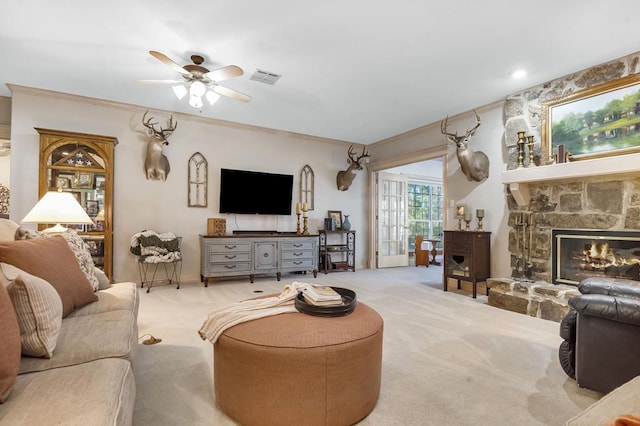 carpeted living room with ceiling fan, a stone fireplace, and ornamental molding