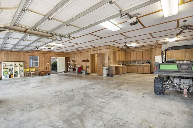 garage featuring ceiling fan, wood walls, and a garage door opener