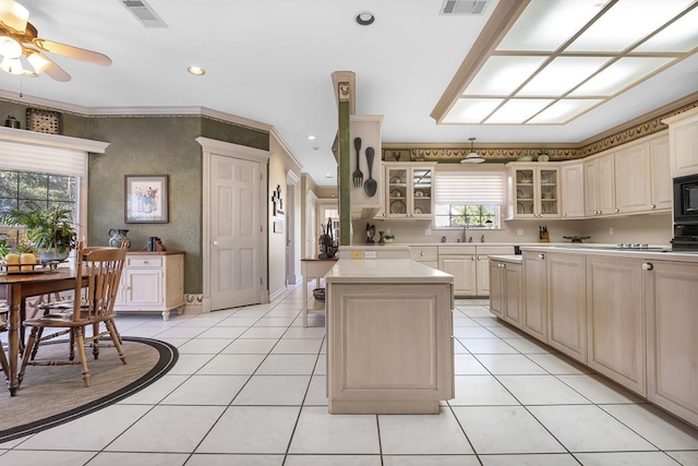 kitchen with ornamental molding, black microwave, cream cabinets, light tile patterned floors, and a kitchen island