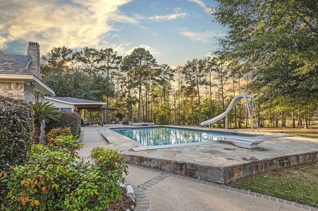 pool at dusk featuring a diving board, a patio, and a water slide