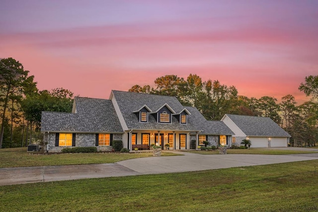 cape cod-style house featuring central AC, a yard, and a garage