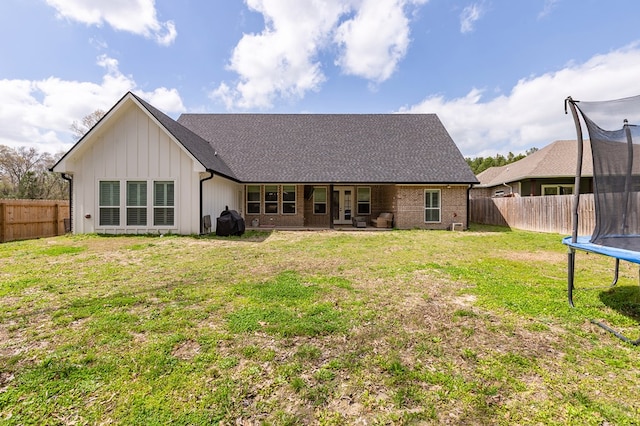 rear view of property featuring a yard, a trampoline, board and batten siding, and a fenced backyard