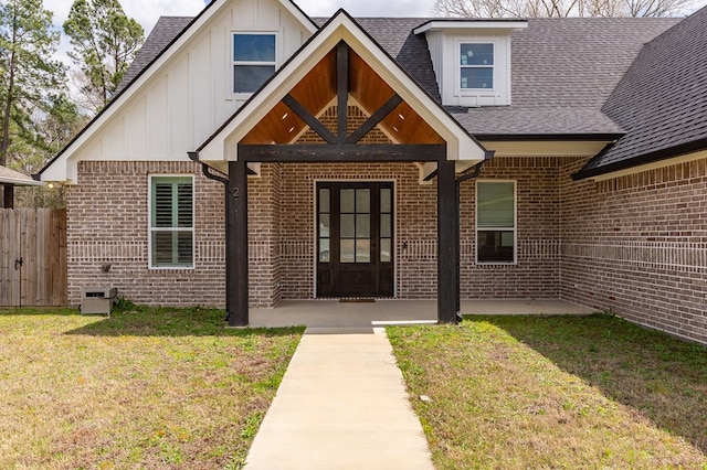 property entrance featuring board and batten siding, a lawn, brick siding, and roof with shingles