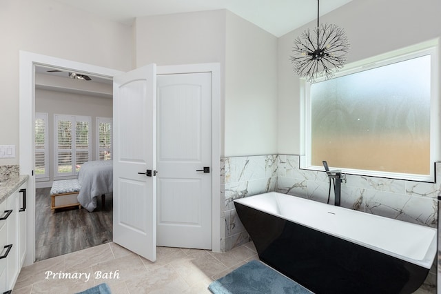 ensuite bathroom featuring a wainscoted wall, connected bathroom, tile walls, an inviting chandelier, and a soaking tub