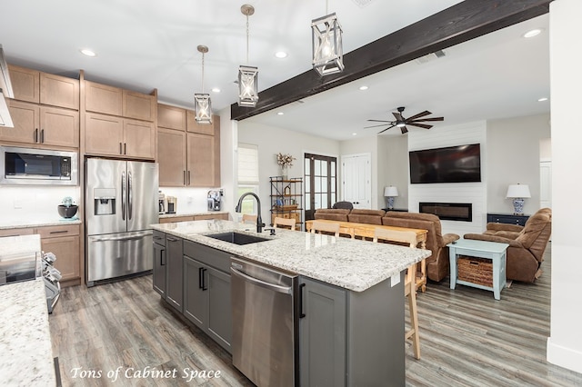 kitchen featuring beam ceiling, light wood-style flooring, a sink, stainless steel appliances, and a large fireplace