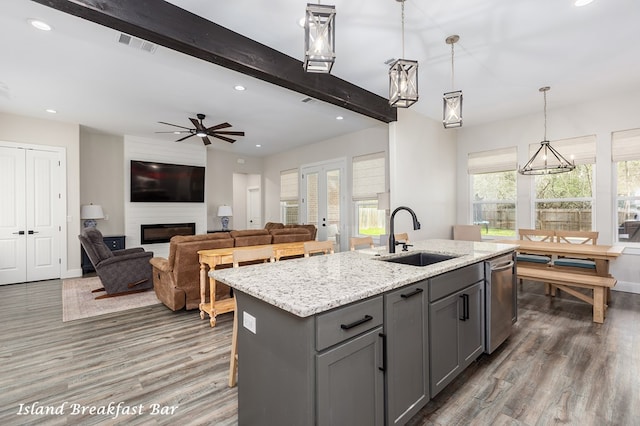 kitchen featuring beamed ceiling, gray cabinetry, a sink, a fireplace, and dishwasher