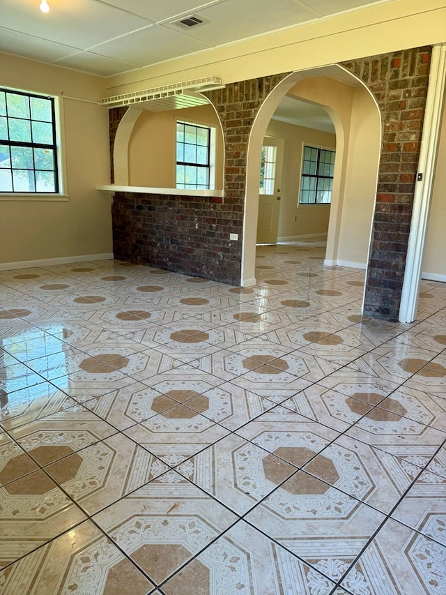 spare room featuring arched walkways, a wealth of natural light, baseboards, and visible vents