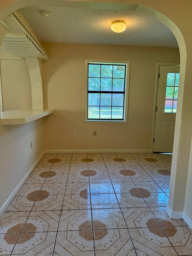 interior space featuring arched walkways, a textured ceiling, baseboards, and light tile patterned floors